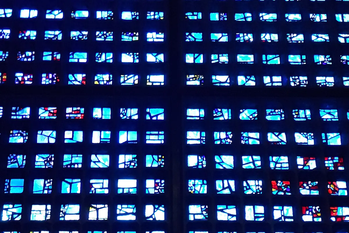 Nahaufnahme der Schiffswand der Gedächtniskirche, ein Raster kleiner blauer Glasscheiben in dunklen Betonrahmen mit verstreuten roten und weißen Sprenkeln