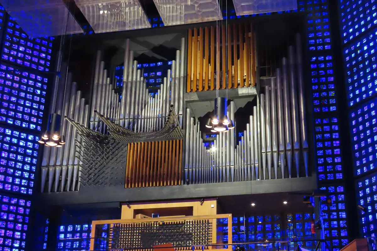 Die Orgel der Gedächtniskirche vom Boden des Kirchenschiffs aus gesehen: ein grau-goldenes Pfeifengehäuse auf einer Empore, umrahmt von Wänden aus kleinen blauen Glasscheiben