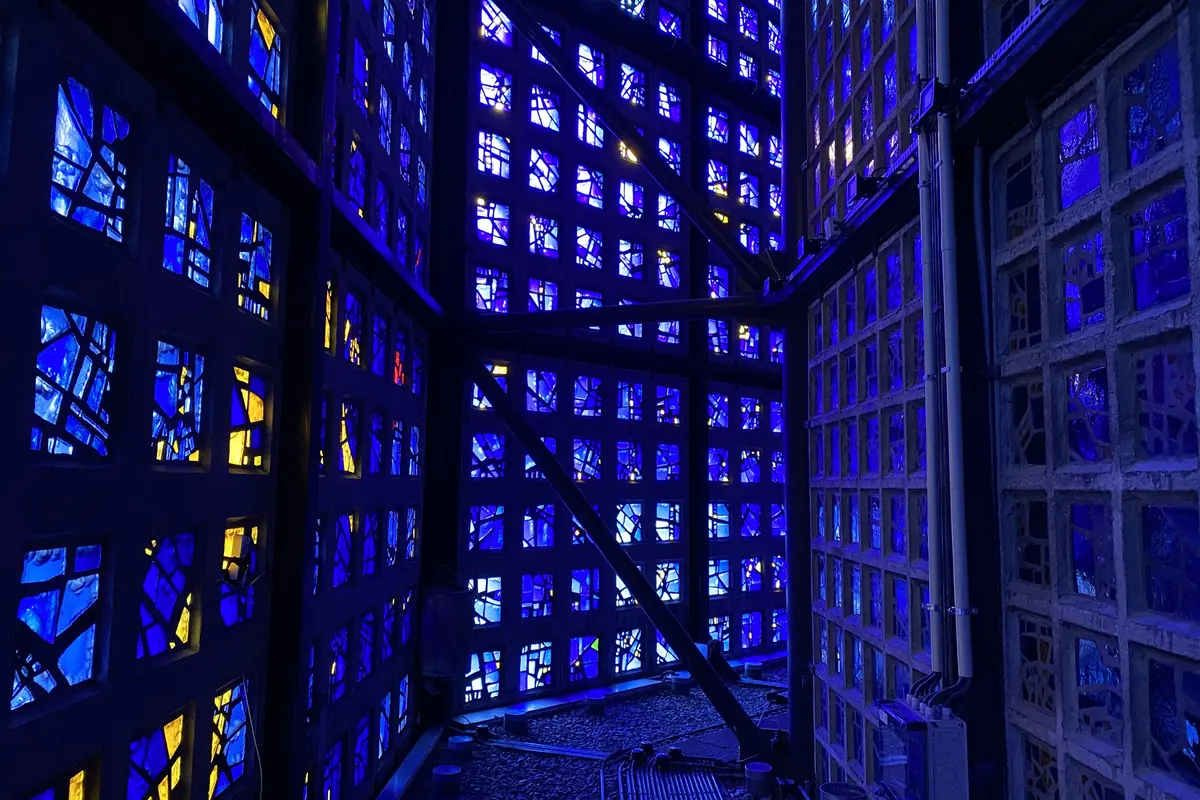Der schmale Gang zwischen der Innen- und Außenwand der Gedächtniskirche, gesäumt von blauen und gelben Glasscheiben in wabenförmigen Betonrahmen